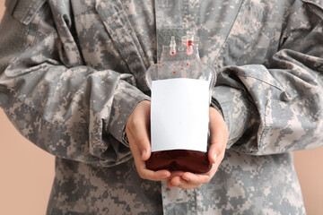 Soldier holding blood pack on beige background, closeup. Blood donation concept