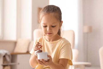 Cute little girl with spoon eating yogurt at home
