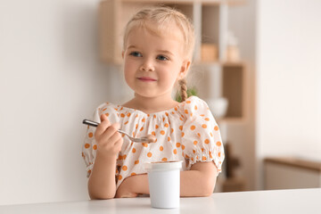 Cute little girl with spoon and yogurt at home