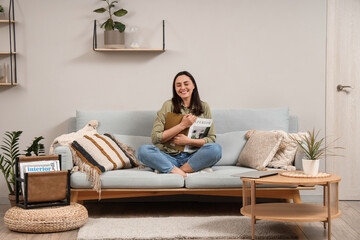 Obraz premium Young woman reading magazine on grey sofa near light wall at home