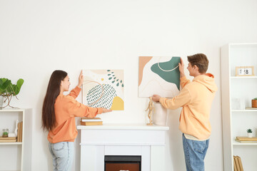 Young couple hanging paintings on wall above fireplace at home, back view