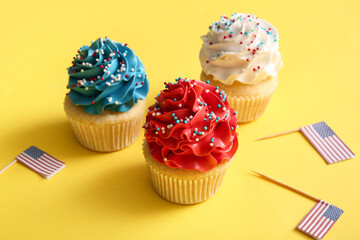 Tasty patriotic cupcakes with USA flags on yellow background. American Independence Day