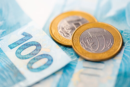 Real - BRL, moeda corrente do Brasil. Moedas de 1 Real e c&eacute;dulas banc&aacute;rias de 100 reais em fotografia macro. Economia brasileira, neg&oacute;cios e finan&ccedil;as.