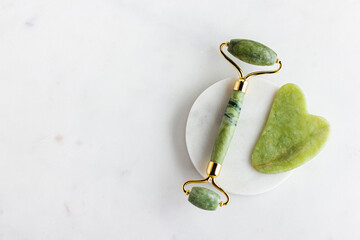 Green jade roller massager for face on white marble.