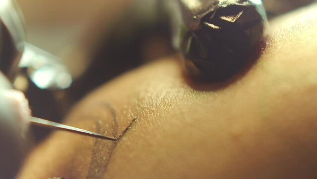 Hands of tattoo artist in sterile gloves puncturing skin and inserting black ink pigment into dermis with needle. Extreme close-up shot