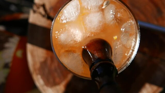 A very immersive POV of a person muddling a Caipirinha cocktail. Close-up of a Caipirinha glass on the table. Mixing a Caipirinha recipe with a wooden muddler: cacha&ccedil;a, tangerine, sugar and ice cubes 