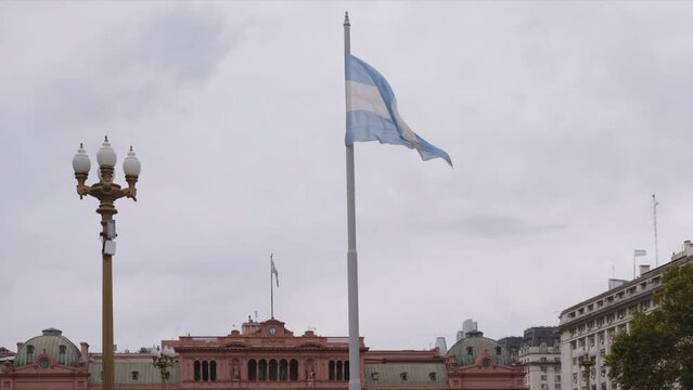 an afternoon shot of the argentine flag unfurling in front of the historic casa rosada in buenos aires, argentina