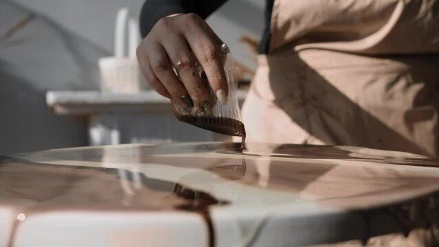 Process of creating an abstract painting using brown epoxy resin is a fascinating one. The craftswoman carefully pours the paint onto the canvas, creating a unique and beautiful work of art. Close up