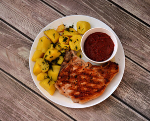 Grilled pork entrecote and boiled potatoes sprinkled with dill on a wooden table.