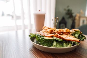 Sandwich bubble waffle with meat, cheese and herbs in a plate opposite a milkshake.