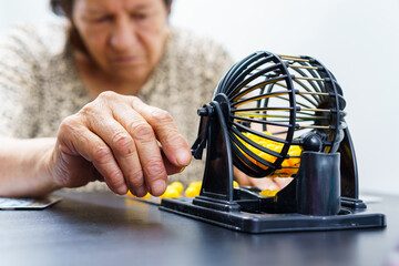 an elderly woman alone playing bingo, shuffling some ballots with a bingo machine