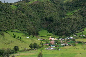 Obraz premium Small Catholic church next to some small farms at the foot of a mountain in a Colombian landscape.