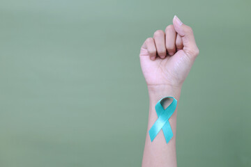 Hand With Teal Awareness Ribbon Clenched Fist Showing Fight Against Cervical Cancer Over Green...