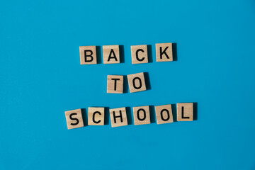 Educational greeting announcement for students and teacher. Saying BACK TO SCHOOL text on wooden blocks on colorful blue background. Top view flat lay Concept of new school year. Minimalistic 