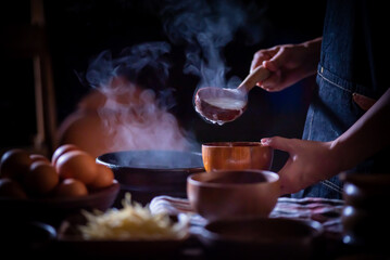 A porridge shop at night on the side of the road as the cook uses a wooden ladle to scoop porridge into a wooden bowl in a retro style. There were eggs and sliced ​​ginger placed on the table.