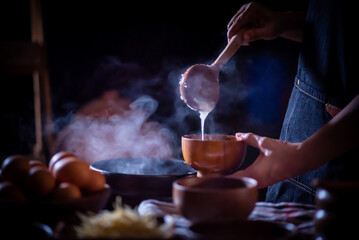 A porridge shop at night on the side of the road as the cook uses a wooden ladle to scoop porridge...