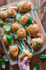 Cheesy Italian pull apart sub sliders with a hand pulling one away.