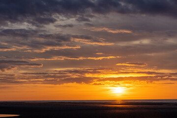 A stunning sunset with golden hues casting light over the ocean horizon and dramatic clouds in the...