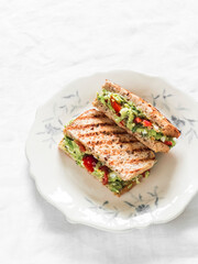 Avocado, egg, red onion, cherry tomatoes, greens spread whole grain grilled bread sandwich on a light background, top view