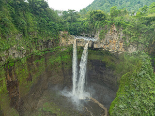 Aerial top view Coban Sriti Waterfall twin Waterfall stream that flows down the valley.The water flowed down into the winding mountain ridges as far as the eye could see. green forest