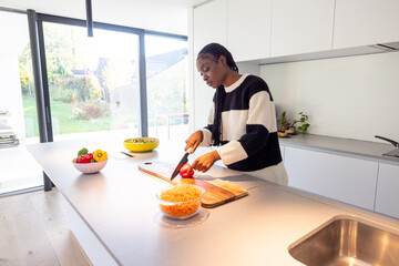 A woman is seen chopping vegetables in a bright, modern kitchen with fresh ingredients on a sunny day