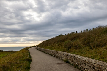 Fototapeta premium This scenic pathway by the sea, under a cloudy sky, is ideal for peaceful walks and appreciating natures beauty