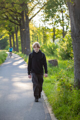 Fototapeta premium Youth enjoying a leisurely walk on a beautiful forest pathway surrounded by lush green trees during a sunny summer day