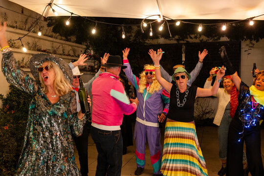 Group of people dancing and celebrating in vibrant costumes at a festive retro-themed outdoor party.