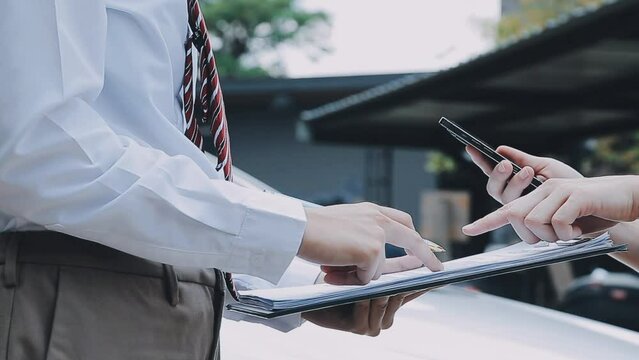 Insurance agent writing on clipboard while examining car after accident claim being assessed and processed