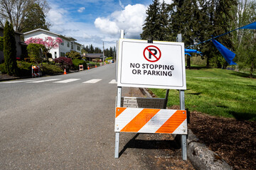 White temporary No Stopping or Parking sign on side of residential street, keeping the road clear for an event on a sunny spring day
