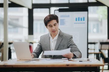 Happy Asian businessman working with accounting documents at table in office Happy man working in modern office