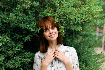 Vibrant redhead woman standing in front of lush green bush in nature