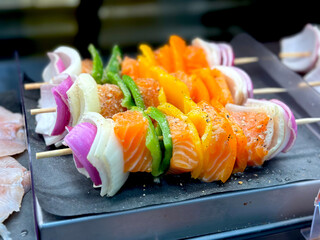 Closeup on Atlantic Salmon Kabobs at Display on a Fresh Seafood Supermarket Section. Wooden Skewers with Red and White Onions and Green and Yellow Bell Peppers. Raw, Refrigerated, Ready to Cook, Deli.