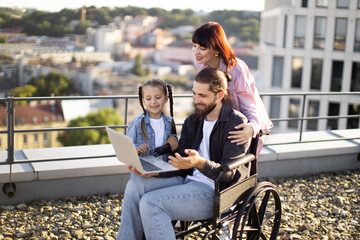 Smiling family with father in wheelchair enjoying outdoor time together. Mother, father, and...