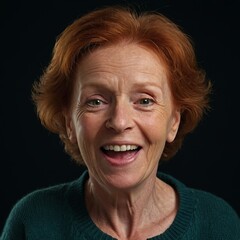 Фn older woman with red hair and fair skin. She smiles and looks directly into the camera. The woman is wearing a green sweater. The background of the photo is dark, which highlights the woman's face