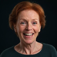 Фn older woman with red hair and fair skin. She smiles and looks directly into the camera. The woman is wearing a green sweater. The background of the photo is dark, which highlights the woman's face