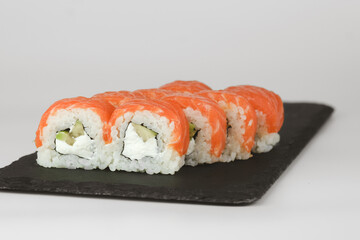 Close-up of salmon avocado sushi rolls on a black slate plate, with a white background