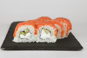 A close up of salmon sushi rolls with cream cheese and avocado filling served on a black slate plate