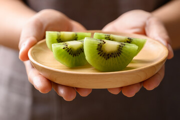 Sliced green kiwi fruit on wooden plate holding by woman hand, Healthy eating