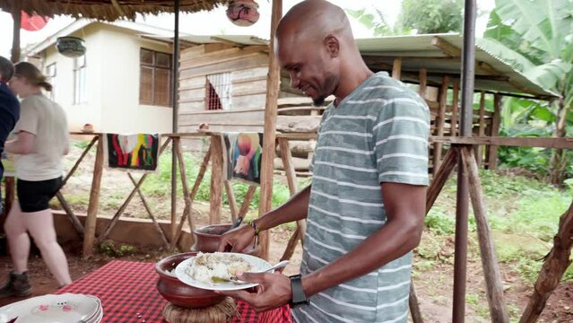 Smiling African man serving Tanzanian traditional dish outside a patio