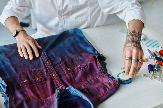 A young man works on restoring a denim shirt, transforming the fabric into a unique, artistic design.