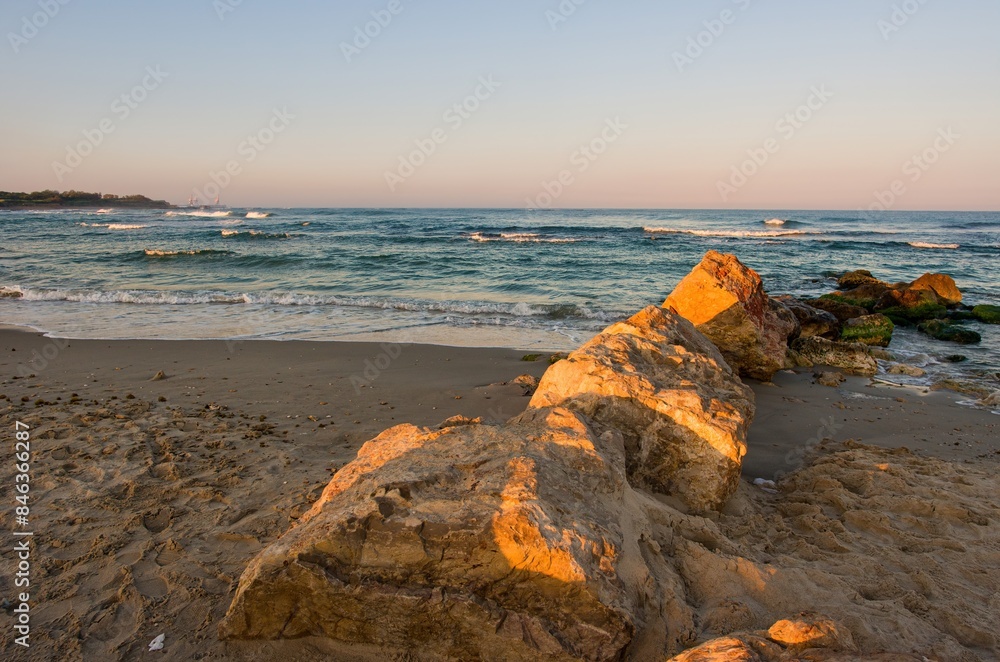 Wall mural Mediterranean coast. Sea surf with white foam of waves. Morning sunrise on the coast of Israel, rocks, sea sand and water.