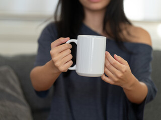 Closeup of female hands with a mug of beverage. A girl in grey t-shirt holding white mug in hand. Mug for PSD mockup. Cropped close-up image of a coffee