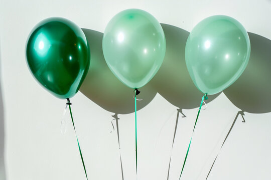 A trio of balloons in shades of green, arranged in a line and casting soft shadows on a white background.