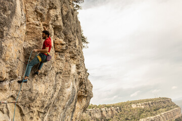 A man is climbing a rock wall with a red shirt on