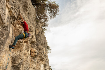 A man is climbing a rock wall with a red shirt and blue pants