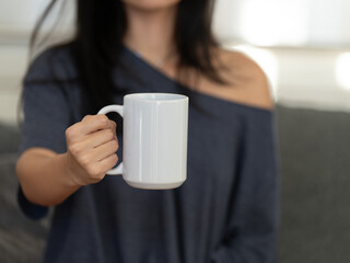 Closeup of a girl in a gray t-shirt holding a blank white coffee mug. Perfect for your design projects. Empty cup in female hands.