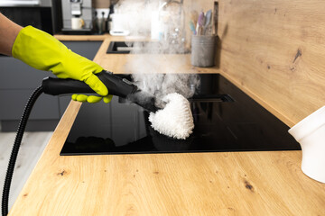 A man's hand in a protective glove cleans a ceramic kitchen stove with steam