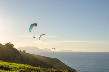 Sunset over the sea in Basque country with people doing paragliding
