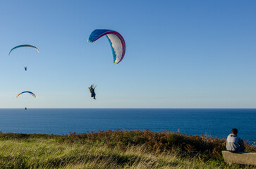 Sunset over the sea in Basque country with people doing paragliding
